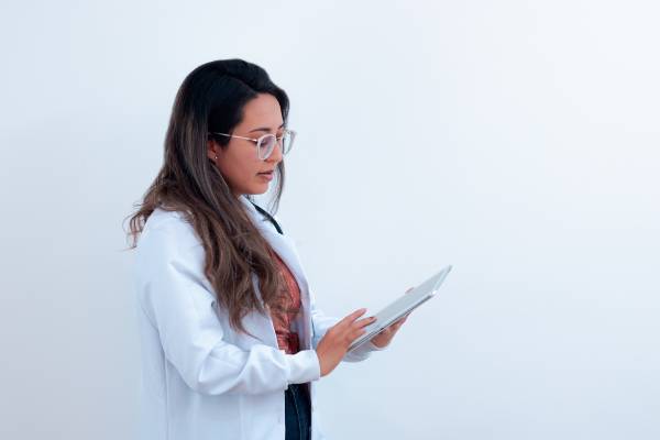 Kvinnlig läkare i profil mot en vit bakgrund som läser från en patientjournal på en vårdcentral med högt anseende i Skåne.